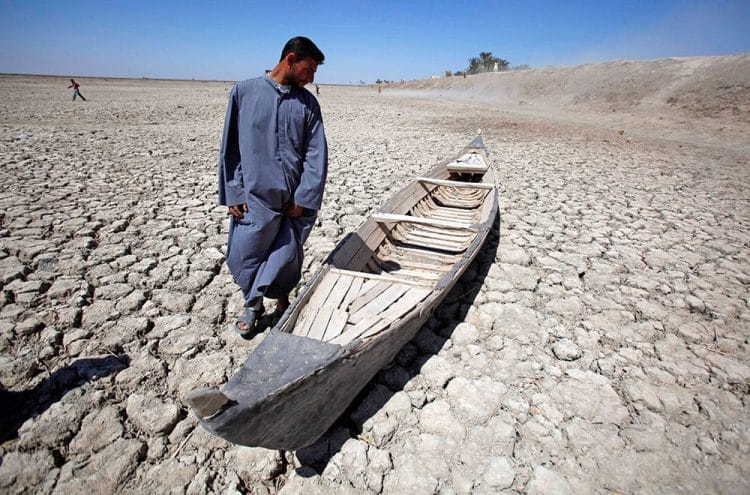 A man stands next to his boat in a dried marsh in Hor al-Hammar in southern Iraq. Photo: AP/Press Association Images/Hadi Mizban