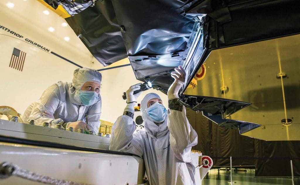Blanket technician Ann Meyer and optical engineer Larkin Carey inspect the protective barrier behind Webb’s primary mirror, December 2018