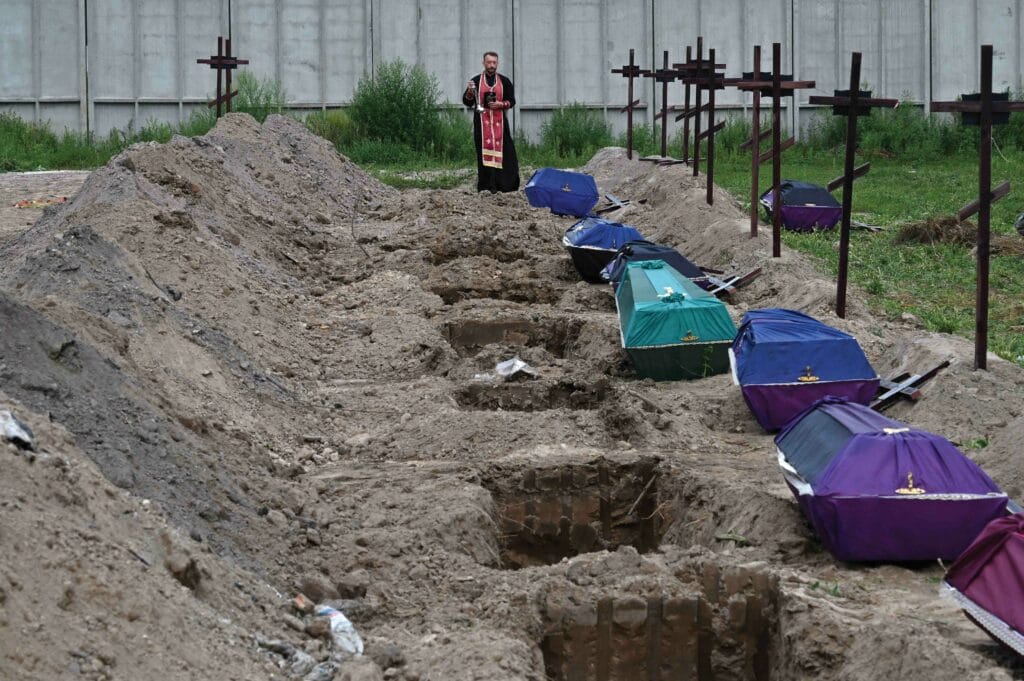  Orthodox priest Andriy Golovin recites a prayer at the graves of unidentified civilians during their funeral at a cemetery in Bucha on 11th August 2022