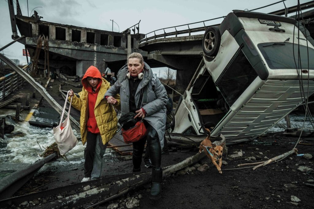 A woman with a child and their dog cross a makeshift walkway over a destroyed bridge during the evacuation from Irpin, 5th March 2022