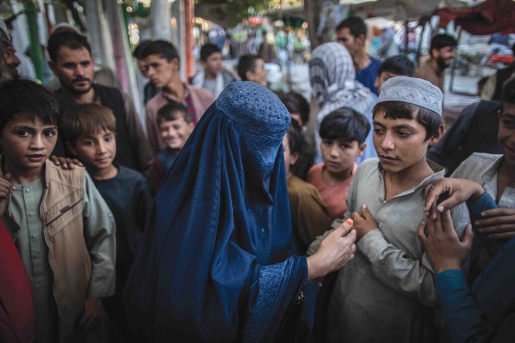 An Afghan woman begging for money is surrounded by men and boys in Kunduz, northern Afghanistan