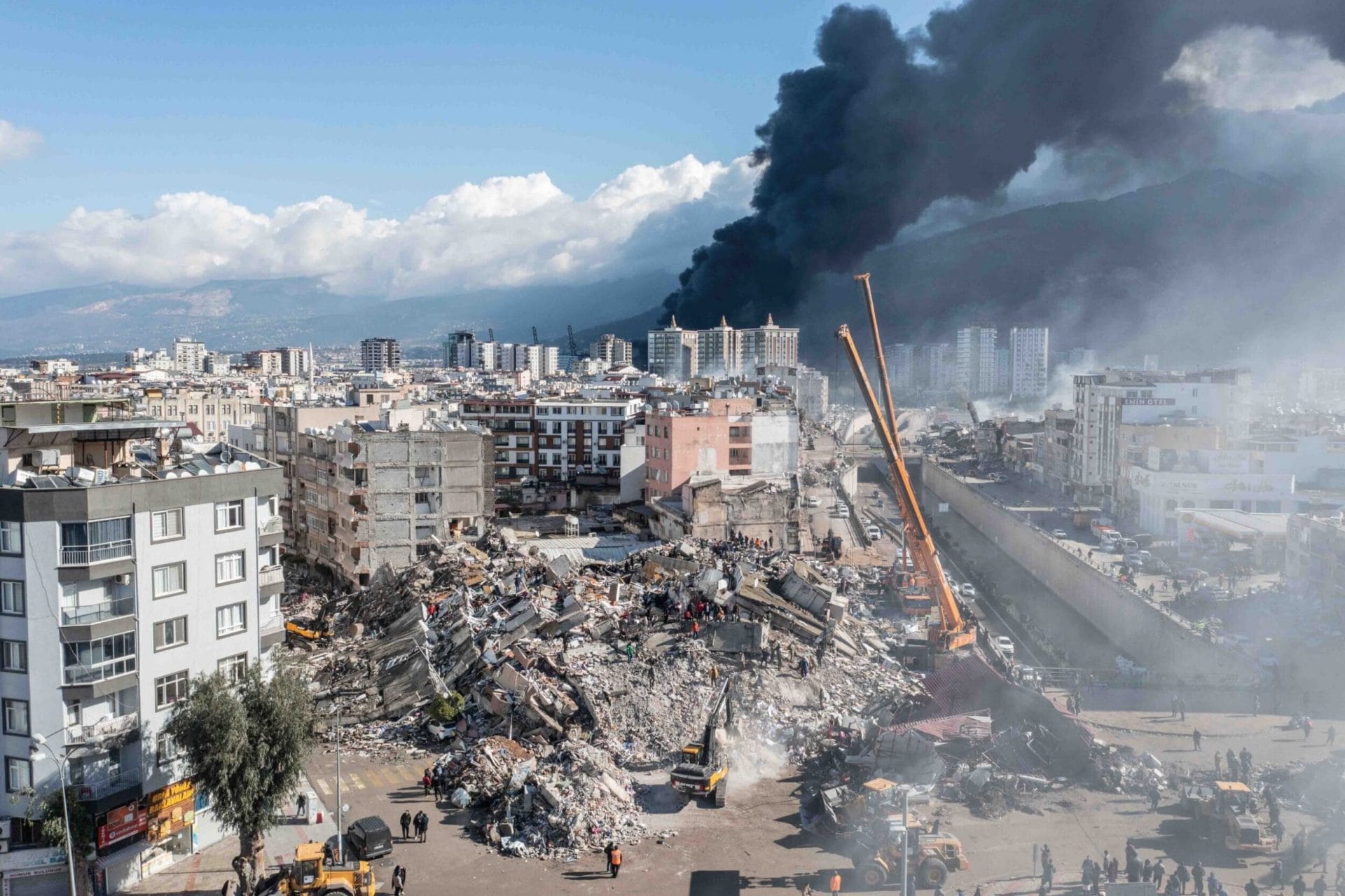  Collapsed buildings in Hatay, with smoke from a fire at the port rising in the distance